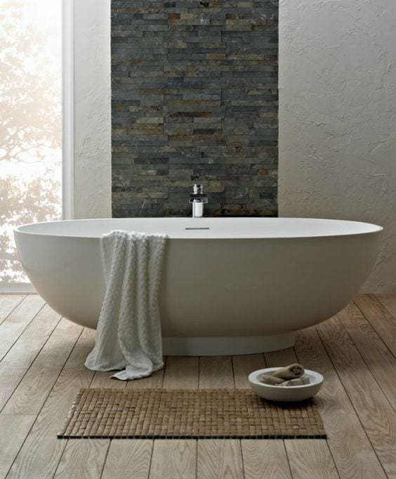 Vrijstaand bad met natuursteen muur en houten vloer